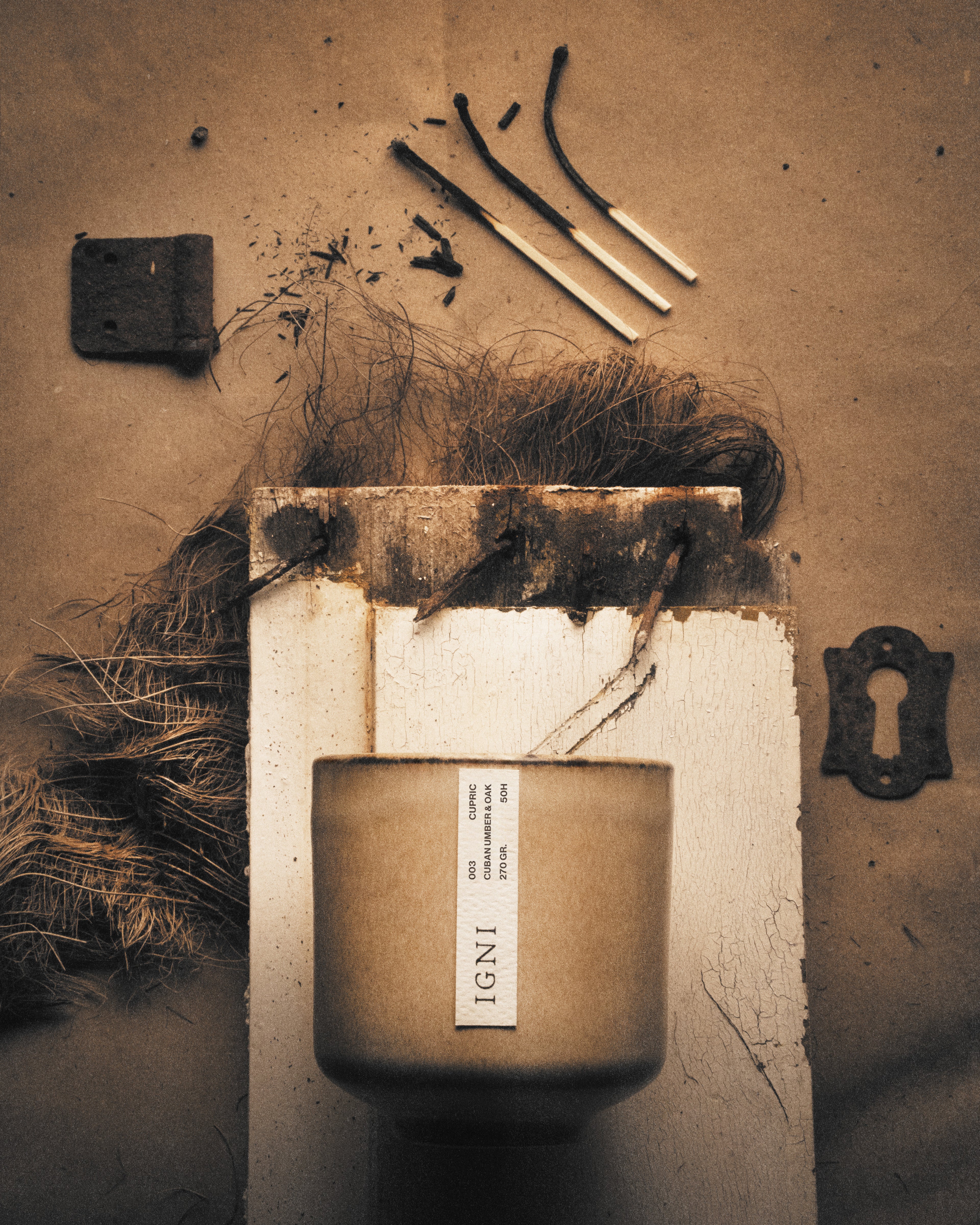 IGNI Cupric Cuban Umber & Oak luxury scented candle in a beige ceramic vessel, styled with burnt matches, charred textures, natural fibers, and rustic earthy materials.