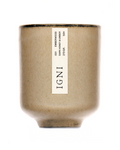 IGNI Emberwood Dark Honey & Umber luxury scented candle in a beige ceramic vessel, styled with layered wood bark, cinnamon sticks, citrus peel, and dark moody textures.