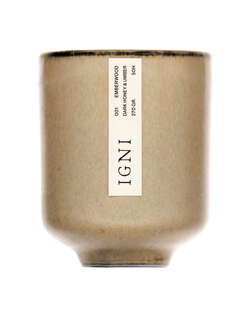 IGNI Emberwood Dark Honey & Umber luxury scented candle in a beige ceramic vessel, styled with layered wood bark, cinnamon sticks, citrus peel, and dark moody textures.